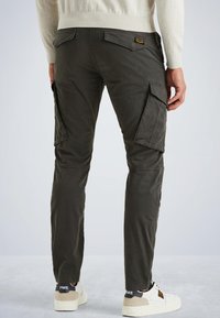 Pantalons cargo verts olive avec plusieurs poches sur les côtés, design cintré, en tissu coton, et un patch logo visible au dos. Associés à des baskets blanches.