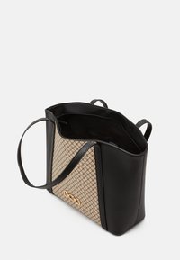 Sac fourre-tout noir et beige avec un motif géométrique en maille, surface texturée, ouverture supérieure et doubles poignées ; orné d'un logo doré.