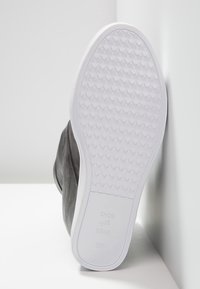 Černá kožená bota s bílou gumovou podrážkou. Vyznačuje se texturovanou podrážkou pro lepší přilnavost. Na podrážce je štítek s nápisem "SHOE THE BEAR," velikost 38.