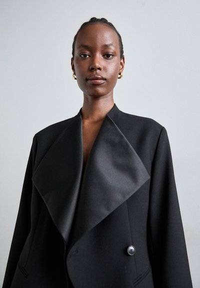 Μαύρο σακάκι με σατέν πέτο, δομημένους ώμους, κλείσιμο με έν αν μόνο κουμπί και πλαϊνές τσέπες, προσφέροντας μια κομψή, ραμμένη σχεδίαση.