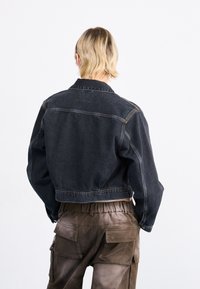 Musthave musta denimpusa, millel on klassikaline krae, nähtavad õmblused ja mugav lõige, koos pruunide elastse vöökohtadega cargo pükstega.