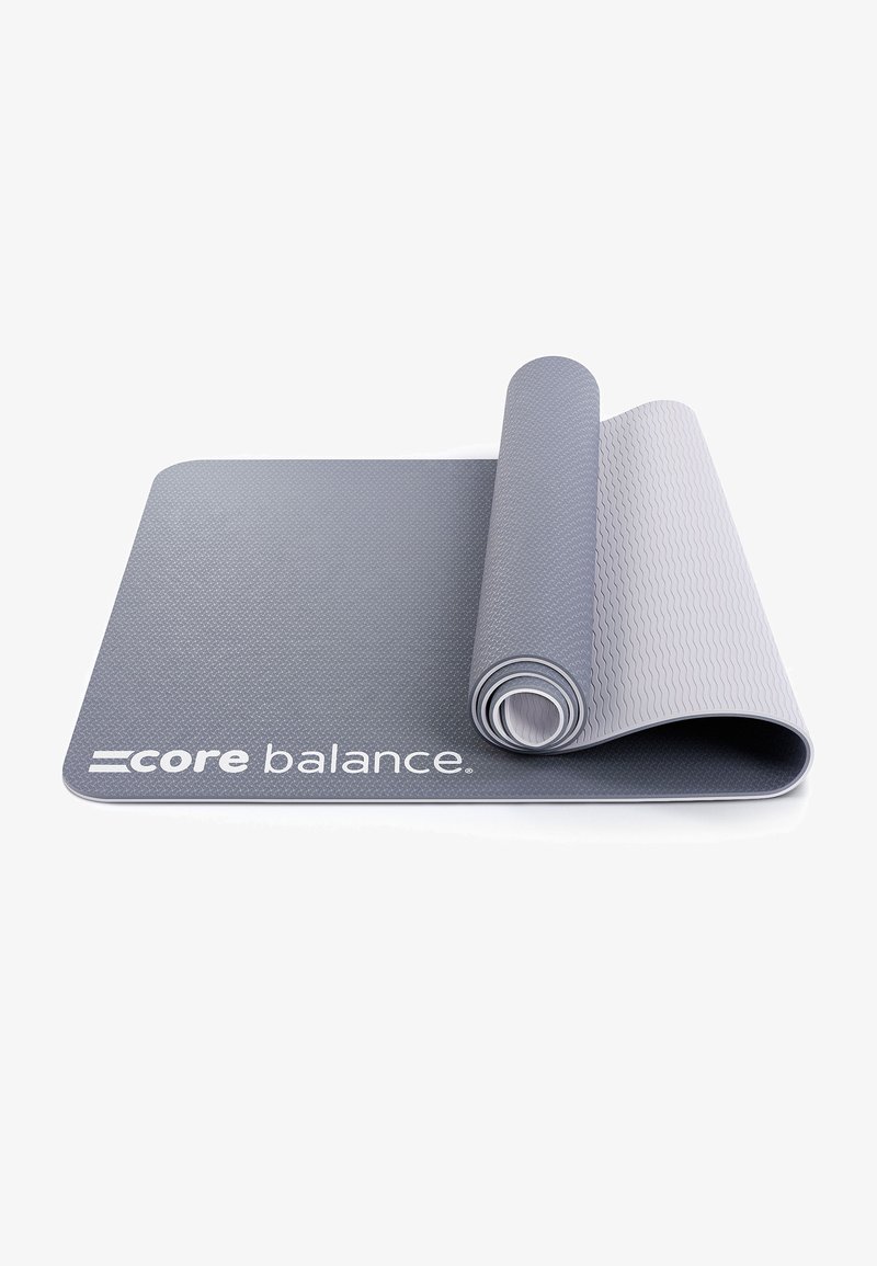 Tappetino da esercizio grigio con superficie testurizzata, arrotolato parzialmente, con il marchio "core balance" stampato in bianco sul bordo inferiore.