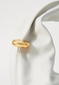 Biała skórzana torebka o miękkim, marszczonym fasonie, podkreślona okrągłym, złotym detalem z logo "FURLA".