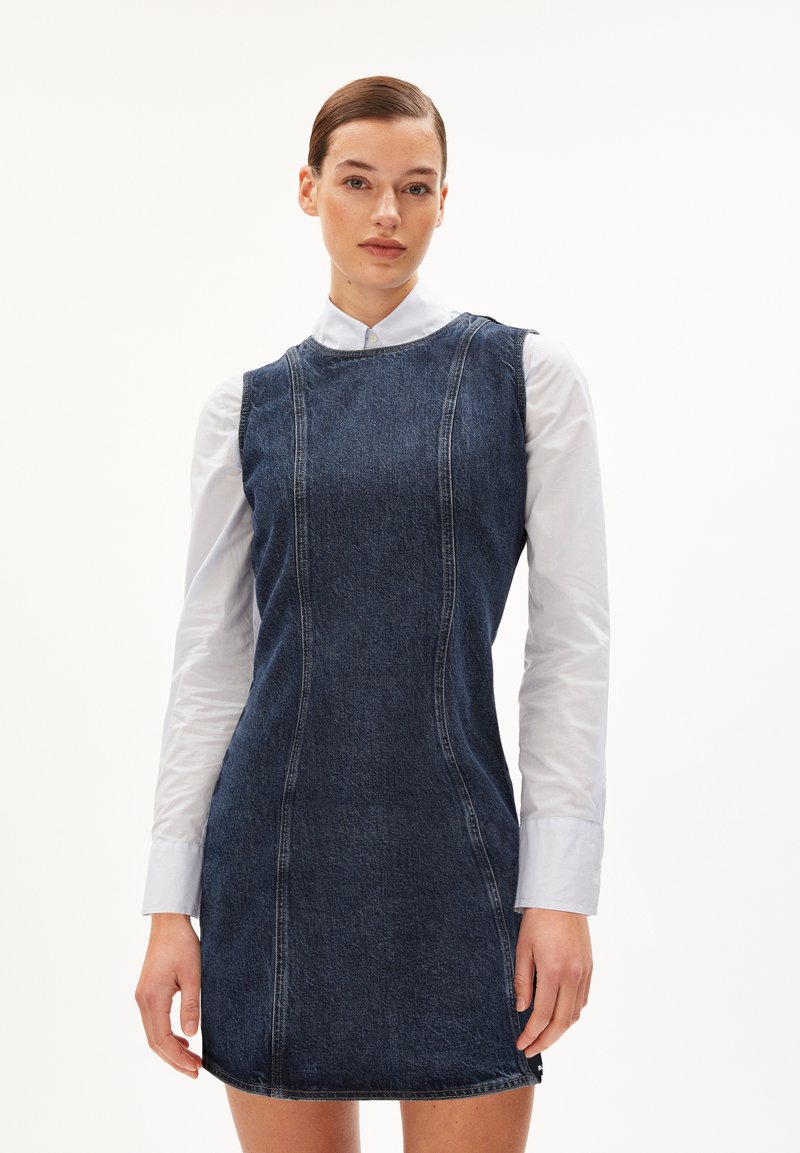 Robe en denim avec une silhouette ajustée, un col rond et des coutures d'épaule. Associée à une chemise blanche à col en dessous.