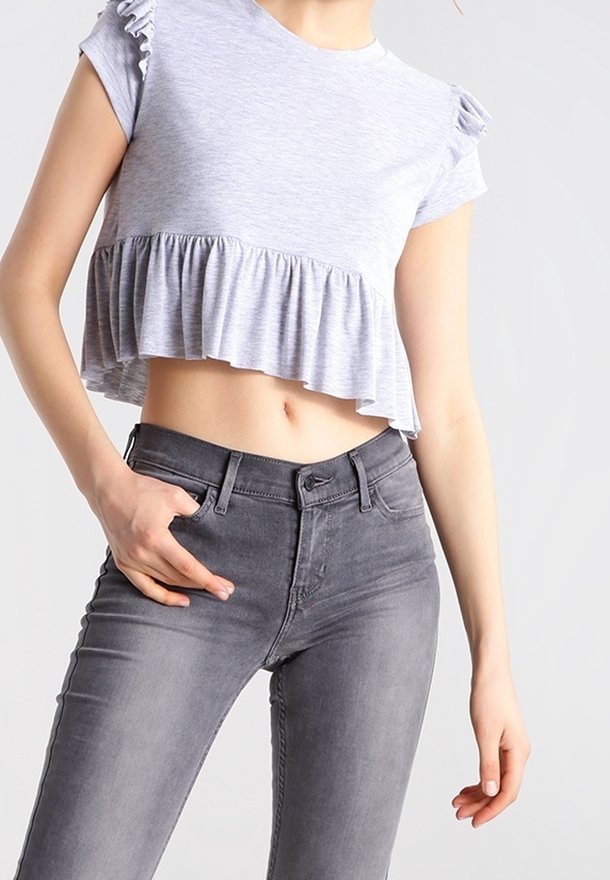 Světlě šedý krátký top s volánkovými rukávy a rozšířeným lemem, doplněný tmavě šedými úzkými džíny s přiléhavým pasem.
