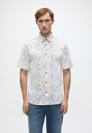 Korte mouwen overhemd met een lichtblauw, wit en rood bloemenpatroon, voorzien van een knoopsluiting aan de voorkant en bruine knopen. Draagt blauw spijkerbroek.