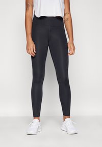 Leggings noirs avec une taille haute, fabriqués en tissu lisse et extensible. Associés à un haut blanc cropped et des chaussures de sport blanches.