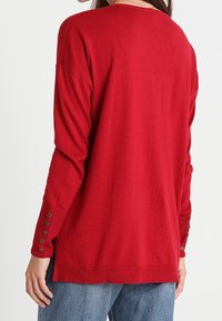 Maglione rosso lavorato a maglia con una vestibilità rilassata, con collo rotondo, maniche lunghe e bottoni decorativi sui polsini.