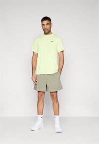 Ανοιχτοπράσινη κοντομάνικη μπλούζα Nike με μαύρο λογότυπο. Μπεζ σορτς με τσέπες, πάνω από το γόνατο. Λευκά αθλητικά παπούτσια και κάλτσες.