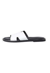 Sandale à bout ouvert avec une tige en cuir blanc présentant des découpes. Semelle noire avec un point de contraste blanc et un design plat.