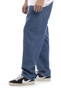 Modre kavbojke s sproščenim krojem, z ravno nogavico, svetlimi odtenki in detajli šivanja. V kombinaciji s črnimi in belimi športnimi copati.