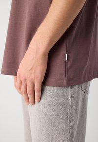 T-shirt de algodão, de mangas curtas, na cor castanho-escuro, com uma bainha arredondada, combinada com jeans de denim texturizado em cinza-claro. Marca mínima na costura lateral.