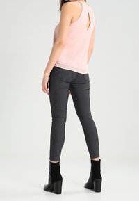 Top senza maniche rosa chiaro con schiena a chiave, abbinato a jeans skinny grigio scuro e stivaletti neri con tacco spesso.