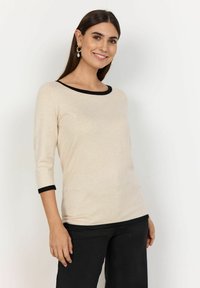 Light beige 3/4 sleeve top with a black neckline and cuffs, made of soft material. Features a round neck and a relaxed fit.
