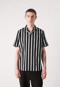 Chemise à manches courtes avec des rayures verticales noires et vert clair, un col en V et une poche à l'avant. Fabriquée dans un tissu lisse.
