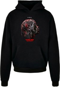 Sudadera negra con bolsillo frontal, que presenta un gráfico de un perfil con trenzas detalladas y patrones en espiral en rojo y gris, con texto debajo.