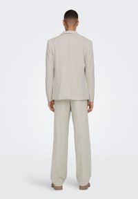 Traje beige claro con un corte entallado, que presenta una chaqueta de un solo corte y pantalones de pierna ancha. Textura suave y diseño minimalista.
