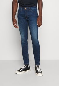 Jeans skinny blu scuro con vita media, design tradizionale a cinque tasche e leggera scoloritura lungo le cosce. Abbinati a sneakers nere alte.