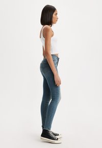 Jeans ajustados de denim en color azul, con un lavado desgastado, diseño de cinco bolsillos y costuras visibles. Combinados con zapatillas altas negras.