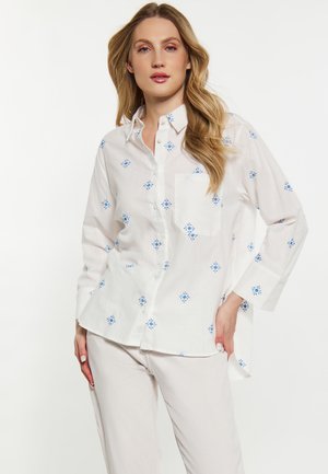 Camicia bianca con motivo floreale blu, caratterizzata da maniche lunghe, una tasca sul petto e una vestibilità rilassata. Tessuto in cotone texturizzato.