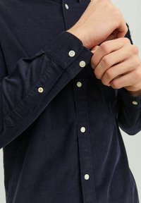 Camisa de pana en color navy con cuello abotonado, que presenta tejido texturizado, puños estándar y botones blancos en la parte delantera y las mangas.