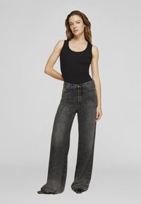 Fekete ujjatlan felső, széles szárú, fekete farmerral, pöttyös mintával. A farmer gombos záródású és elöl zsebekkel rendelkezik.