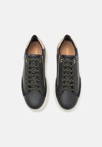 Sneaker in pelle nera con suola bianca, caratterizzati da lacci spruzzati d'oro e dettagli rosa pallido sul tallone e sui lati. Texture liscia in tutto il modello.