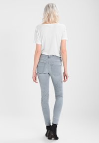 Jeans ajustados de color gris claro con detalles sutiles desgastados, de cintura alta y con bolsillos traseros. Combinados con una blusa blanca de mangas cortas y botas de tobillo.