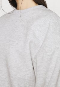 Felpa grigia con tessuto texturizzato, scollatura a girocollo e cuciture delle spalle scese. Il design è semplice, senza motivi né decorazioni.