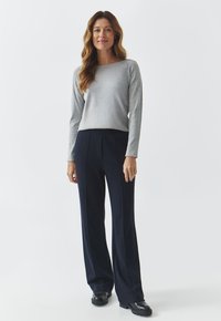 Lichtgrijze long-sleeve top gecombineerd met hoog-gegraafde blauwe broeken. De outfit heeft een relaxte pasvorm en een gestructureerde stof. Zwarte schoenen maken de look compleet.