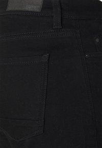 Jeans in denim nero con una leggera vestibilità elastica. Presentano una tasca posteriore, una piccola etichetta in rilievo con logo e cuciture tono su tono per un aspetto uniforme.