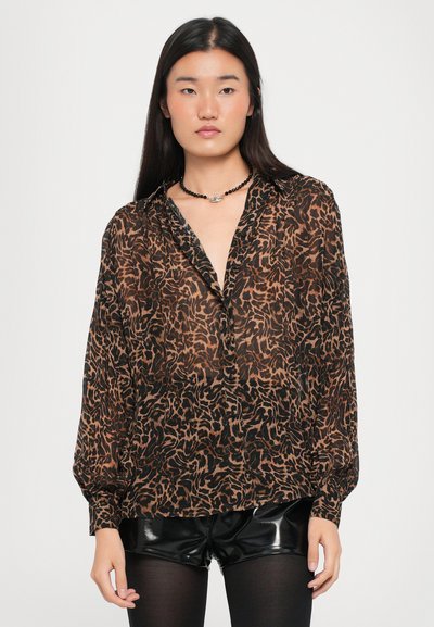 Brun gennemsigtig bluse med sort leopardprint, lange ærmer og dyb V-udskæring. Sammen med skinnende sorte shorts og en sort perlekæde.