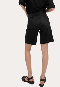 Shorts in denim nero a vita alta con orlo sfrangiato, dotati di tasche posteriori. Abbinati a un top in maglia nera e sandali neri con listini.