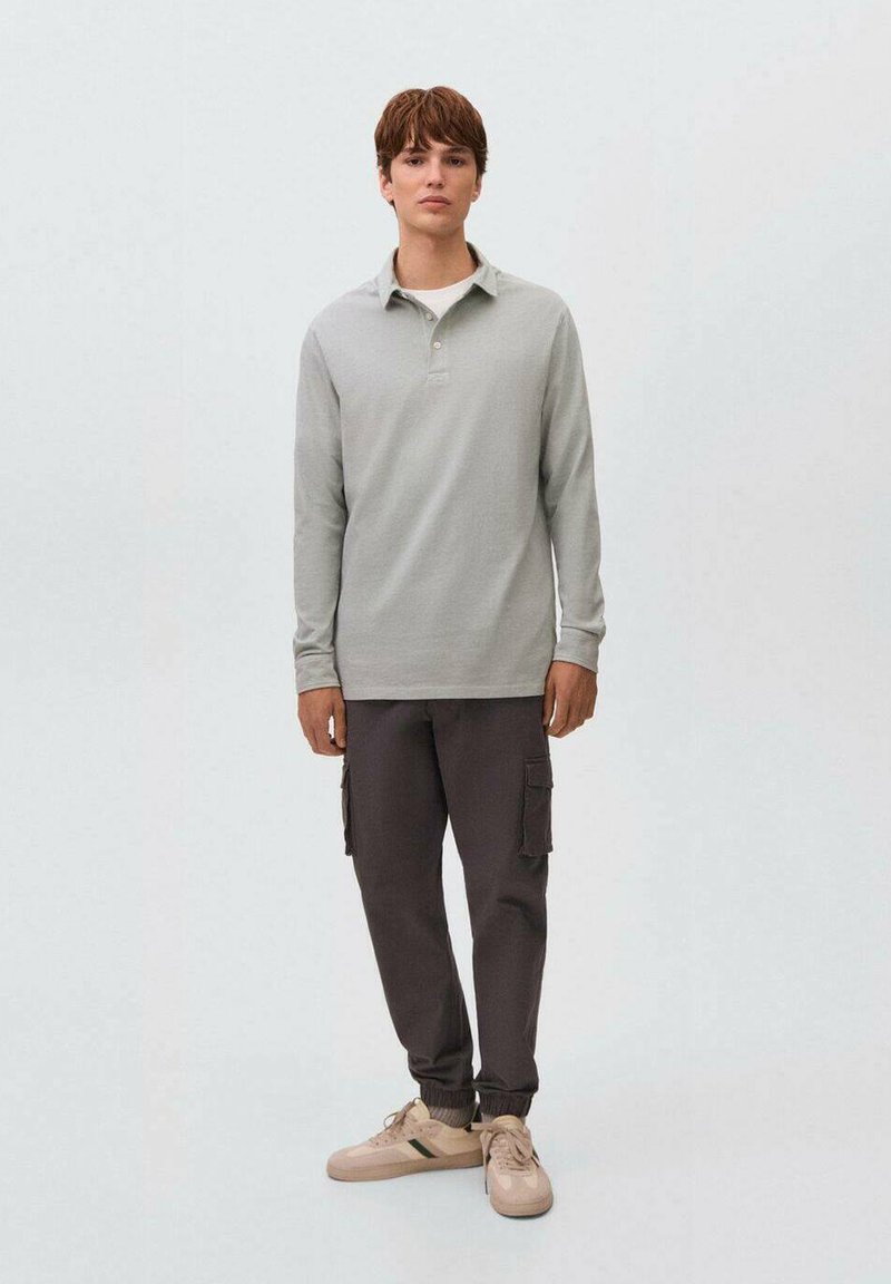 Polo a maniche lunghe grigio chiaro con colletto abbinato a pantaloni cargo grigio scuro e sneakers beige con accenti verdi. Vestibilità semplice e rilassata.