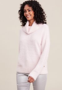 Pull en laine rose flou avec un col cheminée, des manches longues et un ourlet côtelé. Doté d'un petit accent métallique sur le côté. Associé à un pantalon argent.