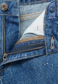 Denim jeans featuring a zip and button closure, orange stitching, and small metallic accents on the front pocket area. Light blue color.