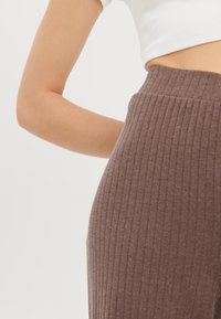 Mörkbruna ribbade stickade byxor med bred midjeresår, med vertikala ränder och en kroppsnära passform.