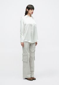 Cămașă albă din satin cu nasturi și guler, asortată cu pantaloni cargo gri deschis, cu mai multe buzunare și croială lejeră. Cizme maro până la gleznă.