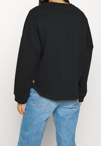 Felpa nera oversize con collo rotondo e spalle scese, realizzata in tessuto morbido, abbinata a jeans denim larghi di colore azzurro chiaro.