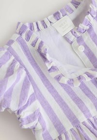 Lila och vit randig babydress med volangkrage och korta ärmar, med knäppning fram och samlat midja. Tillverkad av mjukt tyg.