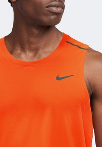 Gros plan d'une personne portant un maillot de sport sans manches orange vif avec un logo Nike noir sur la poitrine.