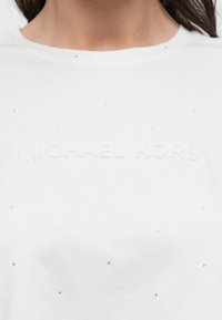 Biały bawełniany t-shirt z wytłoczonym napisem „MICHAEL KORS” oraz małymi, błyszczącymi zdobieniami rozmieszczonymi na tkaninie. Okrągły dekolt.
