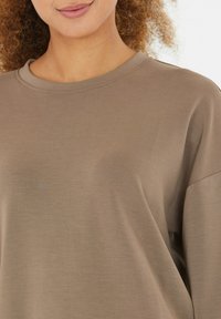 Braun kurzärmliges T-Shirt mit lockerer Passform, rundem Halsausschnitt und glatter Textur. Ein dezent glänzendes Finish verleiht dem Stoff Tiefe.