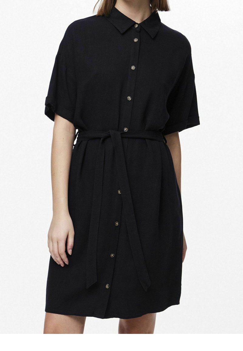 Abito nero a camicia con maniche corte, chiusura a bottoni sul fronte e cintura in vita. Realizzato in un tessuto testurizzato, presenta bottoni metallici e un colletto.