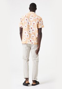 Korte mouwen, oranje bloemenhemel met witte en rode bloemen, gecombineerd met lichtbeige broeken en zwarte sandalen. Eenvoudig ontwerp, casual pasvorm.