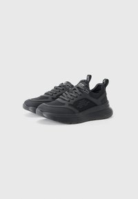 Chaussures de sport noires au design épuré, semelle en caoutchouc texturée, lacets contrastants et détails de marque sur les côtés et la languette.