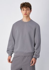 Sudadera gris hecha de una tela suave con puños y dobladillo acanalados, que presenta un pequeño logo bordado en el pecho y pantalones a juego.