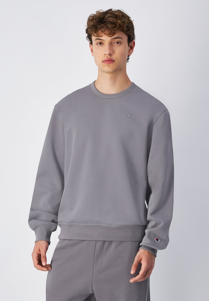 Sudadera gris hecha de una tela suave con puños y dobladillo acanalados, que presenta un pequeño logo bordado en el pecho y pantalones a juego.