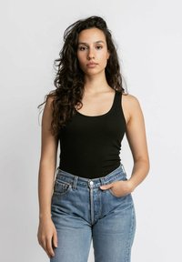 Zwarte mouwloze tanktop, strakke pasvorm, gecombineerd met hoge taille lichtblauwe jeans. Soepele textuur, minimalistische stijl en klassieke silhouet.