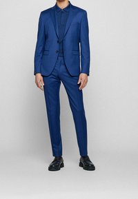 Blå kostym med en figurnära kavaj och skräddarsydda byxor. Slät tyg, strukturerad design, enfärgad kavaj och svarta skor.